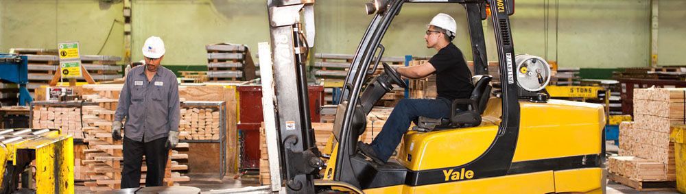 two workers in the Los Angeles steel service center, one is driving a skid loader of equipment